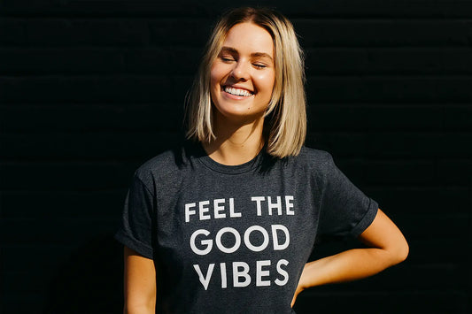 Smiling woman in “Feel the Good Vibes” t-shirt representing a positive wellness mindset and Mitra9 functional drink lifestyle, inspired by kava soda and kratom seltzer culture
