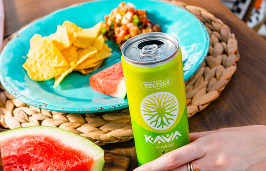 Mitra9 Kava Seltzer can held at outdoor table with watermelon slices, chips, and fresh salsa, showcasing a refreshing kava soda and functional drink for relaxed social moments.