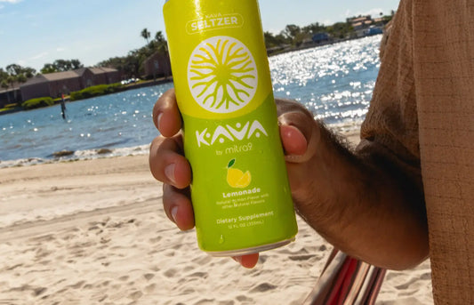 Mitra9 Lemonade kava seltzer can held on a sunny beach by the water, showcasing a refreshing functional kava drink for relaxed summer moments.
