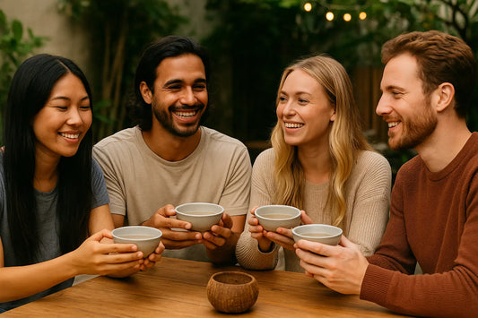 A group of friends sitting at an outdoor table, smiling and holding traditional bowls of kava together, creating a warm and relaxed social atmosphere.